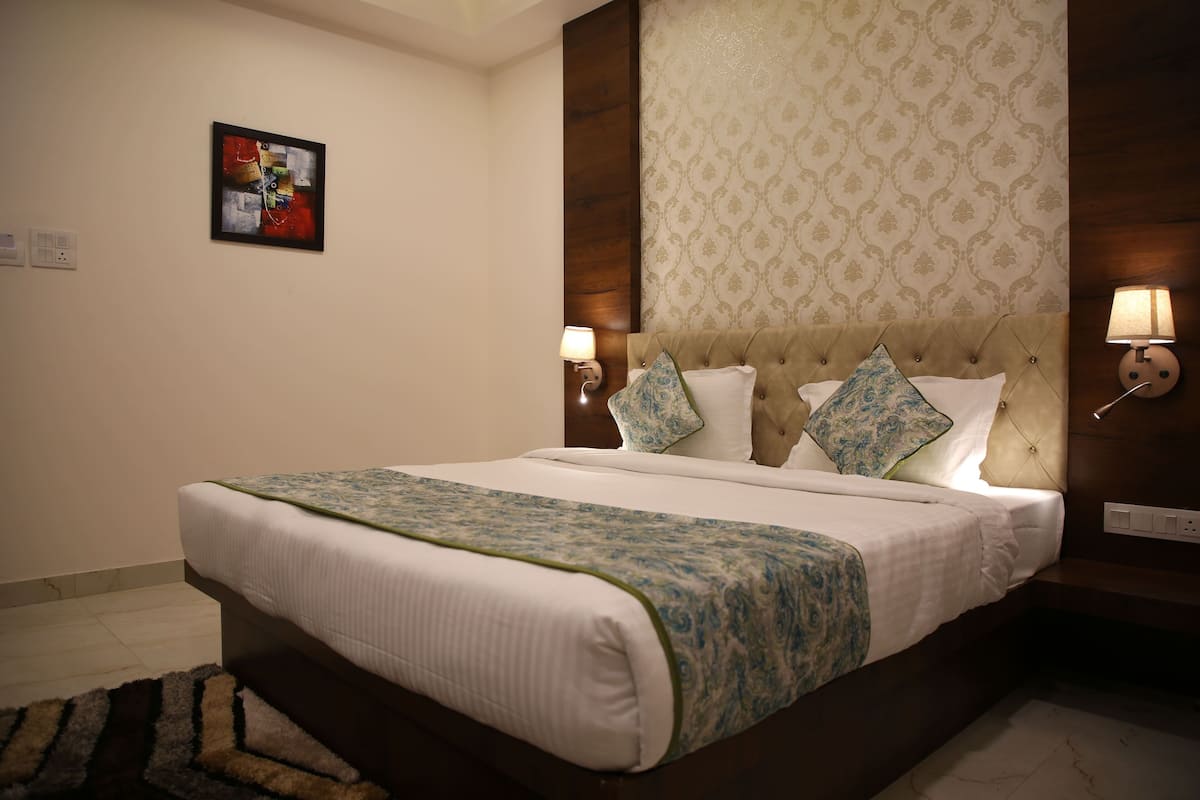 A neatly made bed with a patterned bedspread, a tufted headboard, and two wall-mounted lamps.
