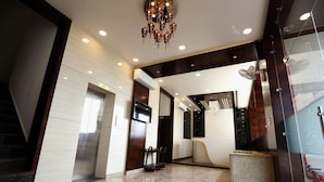 A modern lobby with a marble floor, a chandelier, an elevator, and a glass partition.