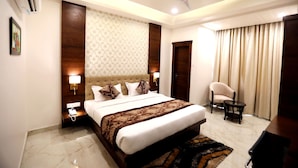 A hotel room with a large bed, a ceiling fan, a bedside table with a lamp, a chair, and a small table.