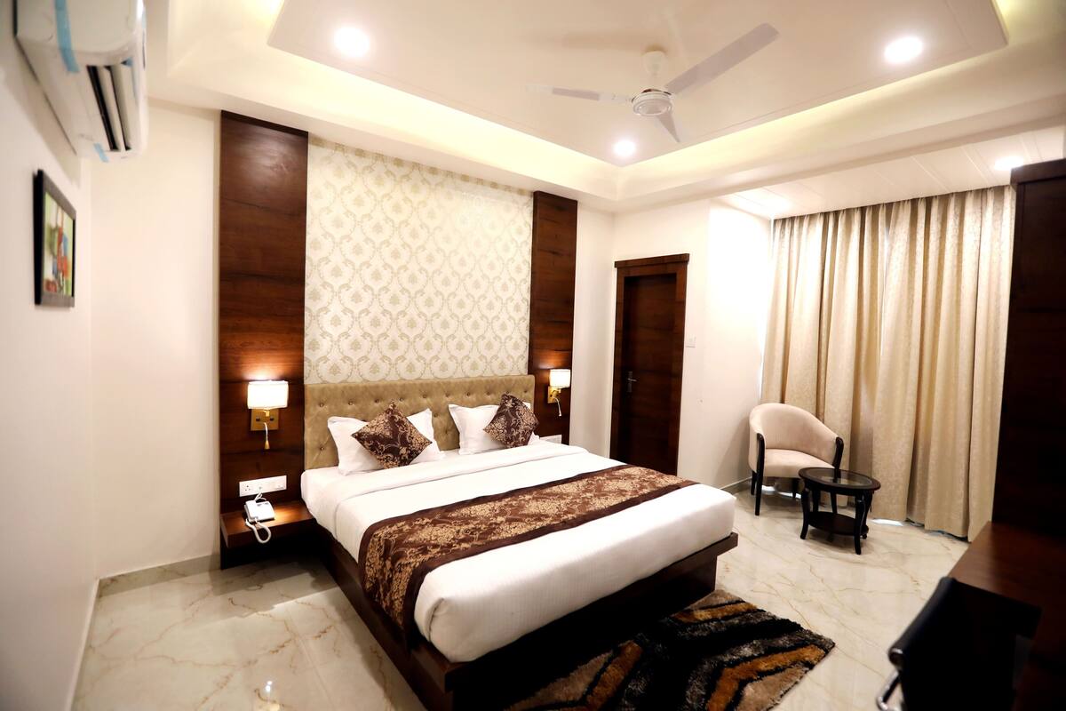 A hotel room with a large bed, a ceiling fan, a bedside table with a lamp, a chair, and a small table.