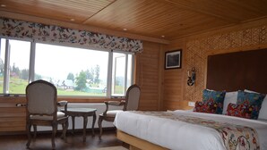 A bedroom with a large bed, two chairs, a small table, and a window with a view of a green landscape. - Kolahoi Green Heights Gulmarg (Baramula)