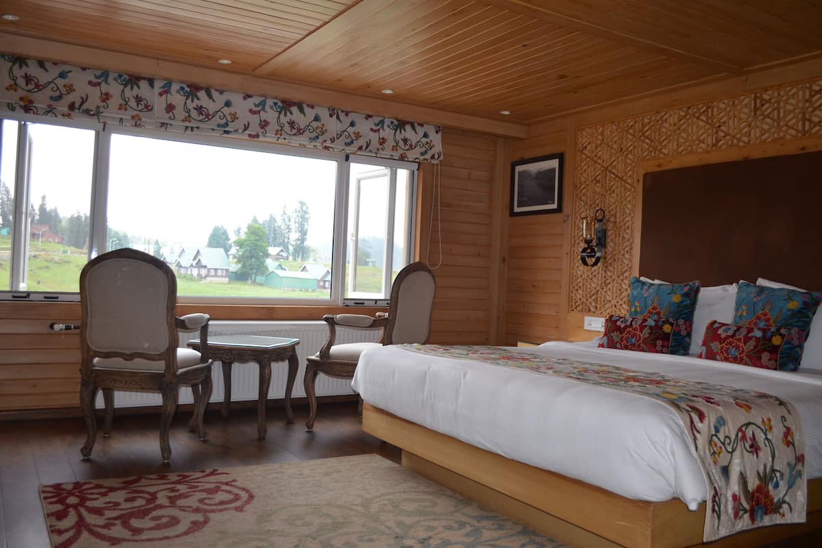 A bedroom with a large bed, two chairs, a small table, and a window with a view of a green landscape.