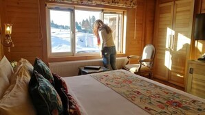 A wooden cabin room with a bed, a chair, and a window overlooking a snowy landscape. - Kolahoi Green Heights Gulmarg (Baramula)