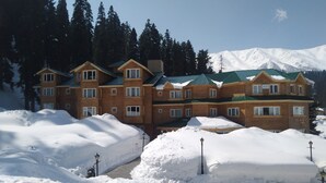 A multi-story wooden building with a green roof, surrounded by snow and trees. - Kolahoi Green Heights Gulmarg (Baramula)