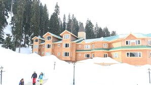 A large wooden building with multiple windows and a green roof, surrounded by snow and trees. - Kolahoi Green Heights Gulmarg (Baramula)