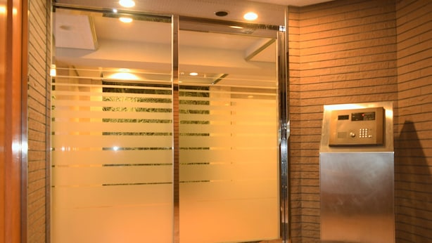 A hotel entrance with a glass door, a reception desk, and a wall-mounted elevator control panel.