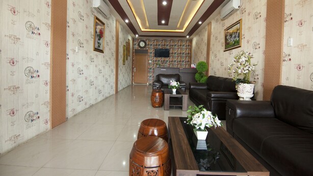 Un vestíbulo de hotel con diseño moderno, que presenta un sofá de cuero negro, una mesa de centro de madera y un jarrón decorativo con flores.