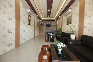 Un vestíbulo de hotel con diseño moderno, que presenta un sofá de cuero negro, una mesa de centro de madera y un jarrón decorativo con flores.