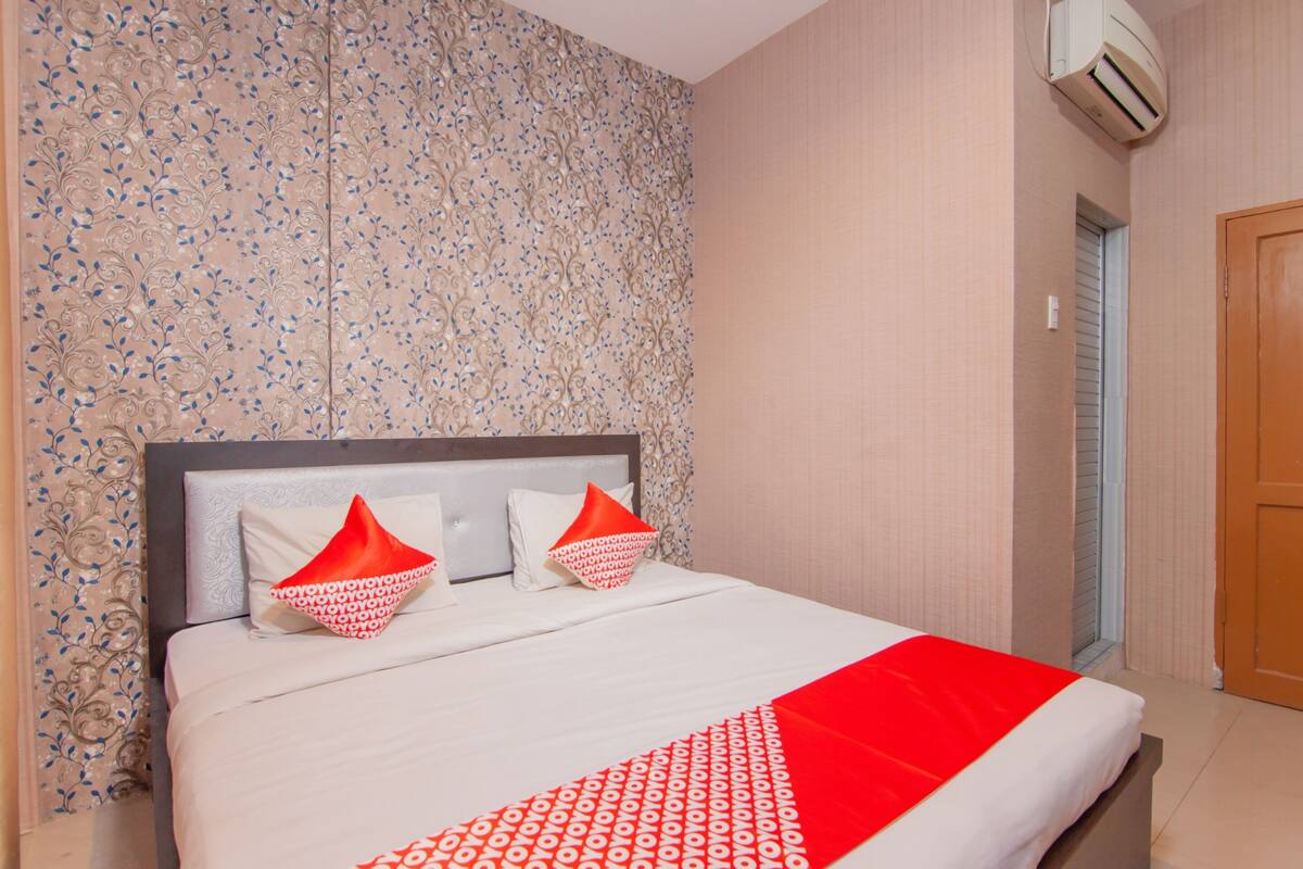 Cama bem arrumada com colcha estampada em vermelho e branco, duas almofadas e cabeceira.