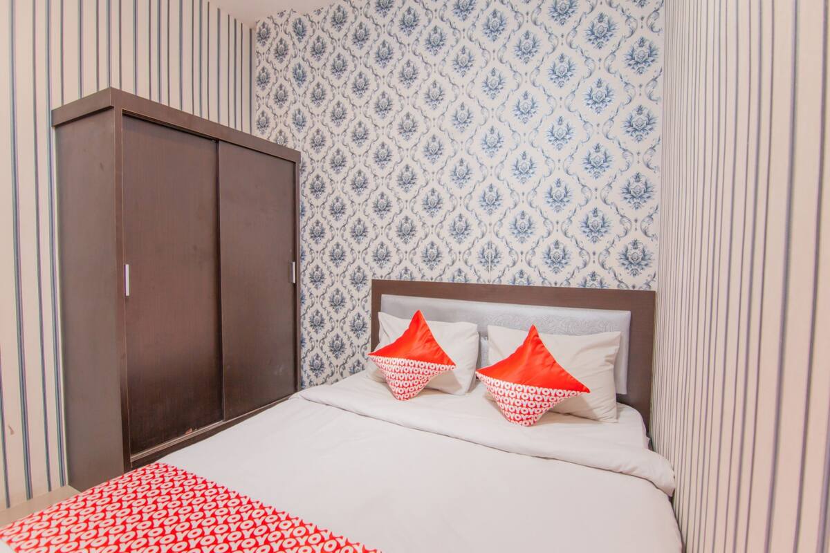 Quarto com cama, duas almofadas, guarda-roupa e papel de parede estampado.