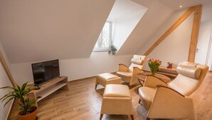 A modern living room with a TV, leather sofas, wooden flooring, and a sloped ceiling. - Hotel Ludwig (Munich)