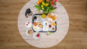 A breakfast tray with various food items, a coffee pot, a vase of tulips, and a wooden table on a wooden floor. - Hotel Ludwig (Munich)