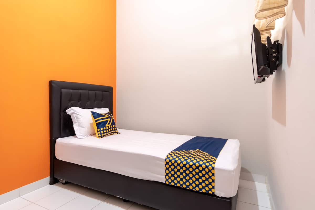 A single bed with a black headboard, white bedding, and a blue and yellow polka dot pillow.