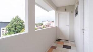 A narrow hallway with a white door, a window with a view of buildings and trees, and a tiled floor. - SPOT ON 2272 Citra Arcade Residence Syariah (Medan)