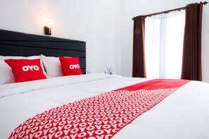 Una habitació d'hotel amb un llit gran, roba de llit vermella i blanca, un capçal de llit, una làmpada penjada a la paret i cortines.