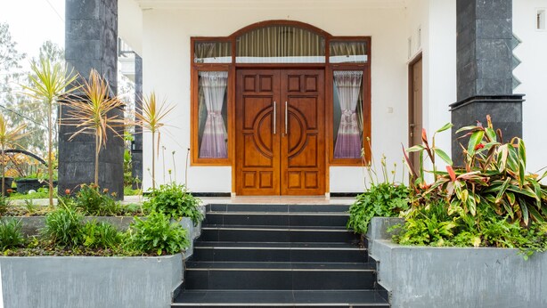 A wooden double door with glass panels and a staircase leading to a white building. - OYO 2169  Anugrah Bromo Homestay (Wonokitri)
