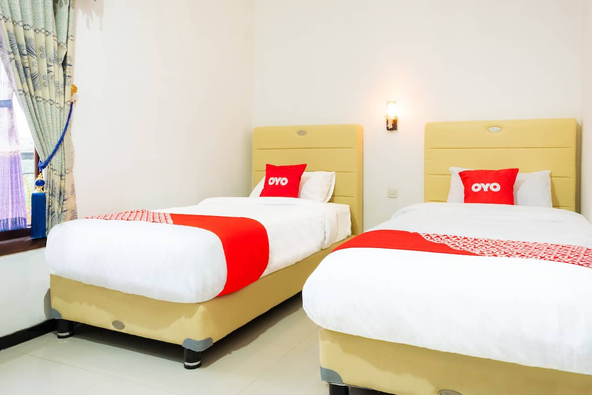 Two beds with yellow headboards, white bedding, and red pillows with the 'OYO' logo.