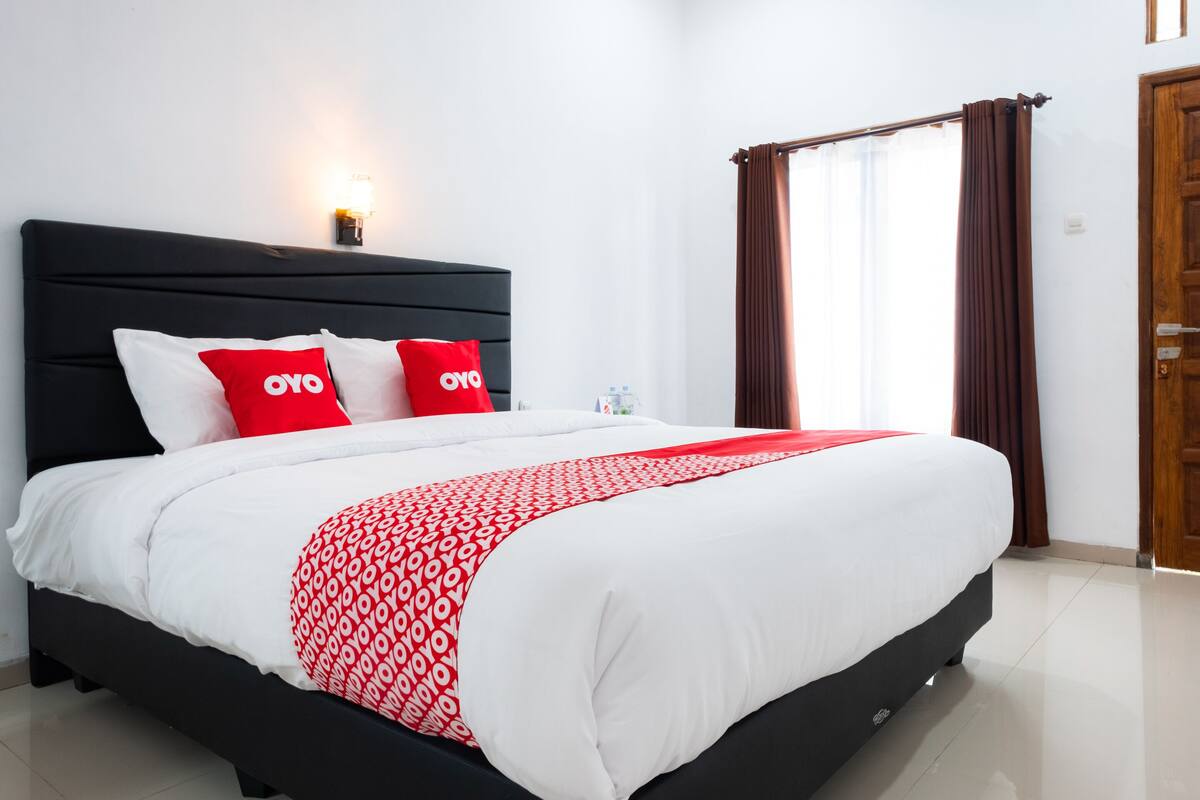 A neatly made bed with a black headboard, white and red bedding, and two red pillows with "OYO" branding.