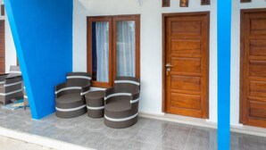 A hotel entrance with a blue wall, two wooden doors, and wicker furniture. - OYO 2169  Anugrah Bromo Homestay (Wonokitri)
