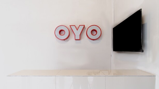Un interior minimalista con un gran letrero iluminado 'OYO' en la pared y un televisor de pantalla plana montado en la pared.