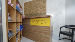 Uma mesa de recepção com um aviso 'SPOT ON', uma prateleira de madeira com diversos objetos e uma cadeira preta.
