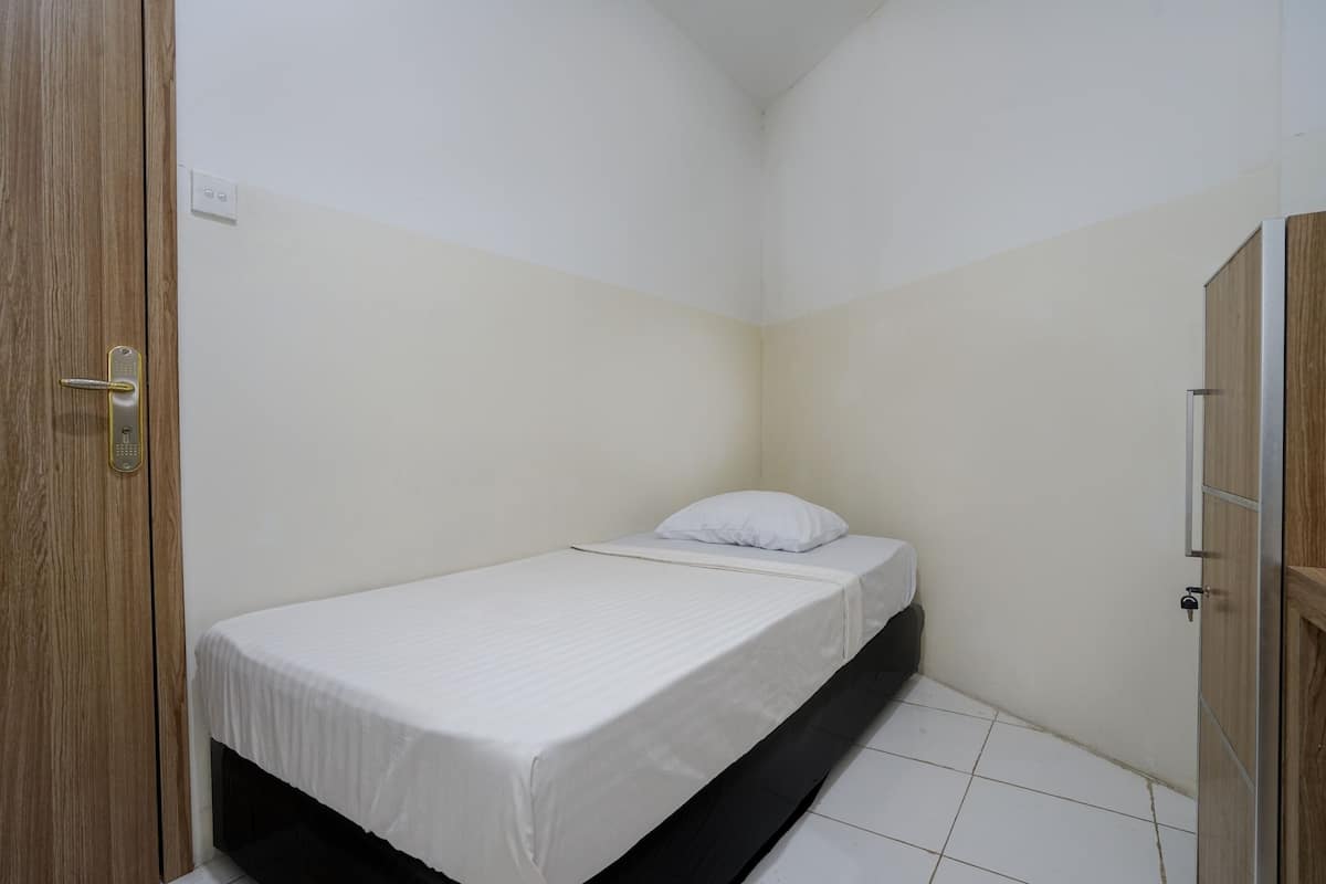 Quarto pequeno com cama de solteiro, porta de madeira e parede branca.