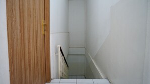 Um corredor estreito, com piso de azulejos, paredes brancas e uma porta de madeira.