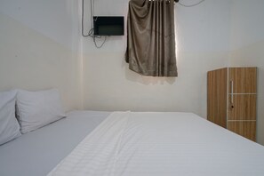 A bedroom with a bed, a wooden wardrobe, and a television mounted on the wall.