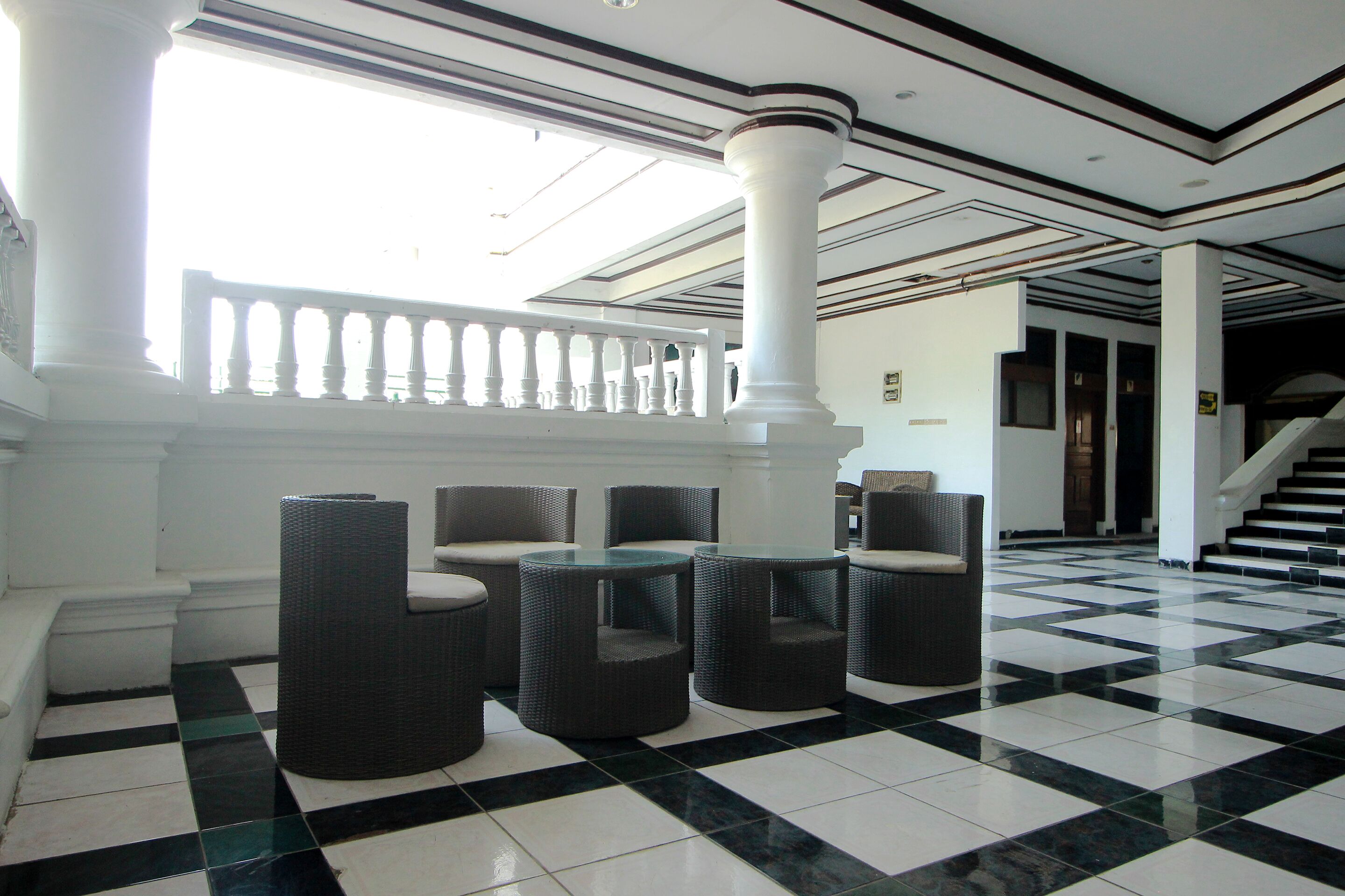 A lobby with checkered flooring, white columns, and wicker furniture.