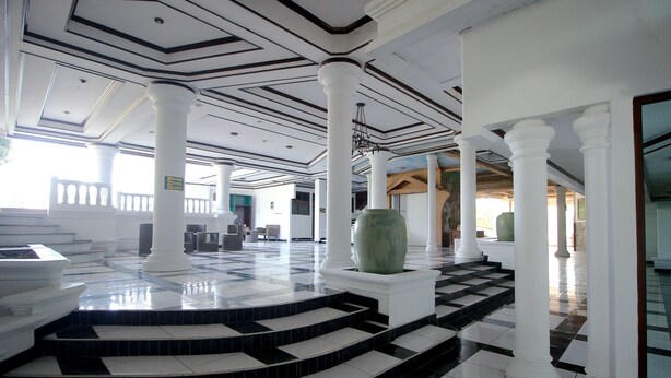 Un vestíbulo imponente con columnas blancas, un gran jarro verde y un suelo a cuadros.