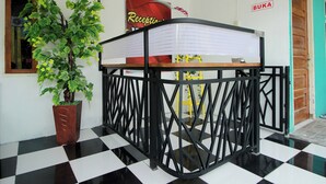 Un comptoir d’accueil avec un sol à carreaux, une plante en pot et une enseigne sur laquelle on peut lire « BUKA ».