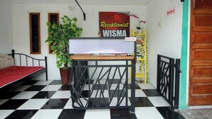 Un espace d’accueil comprenant un comptoir de réception, un lit, une plante en pot et un panneau indiquant : « Réception – réservé au personnel de WISMA ».