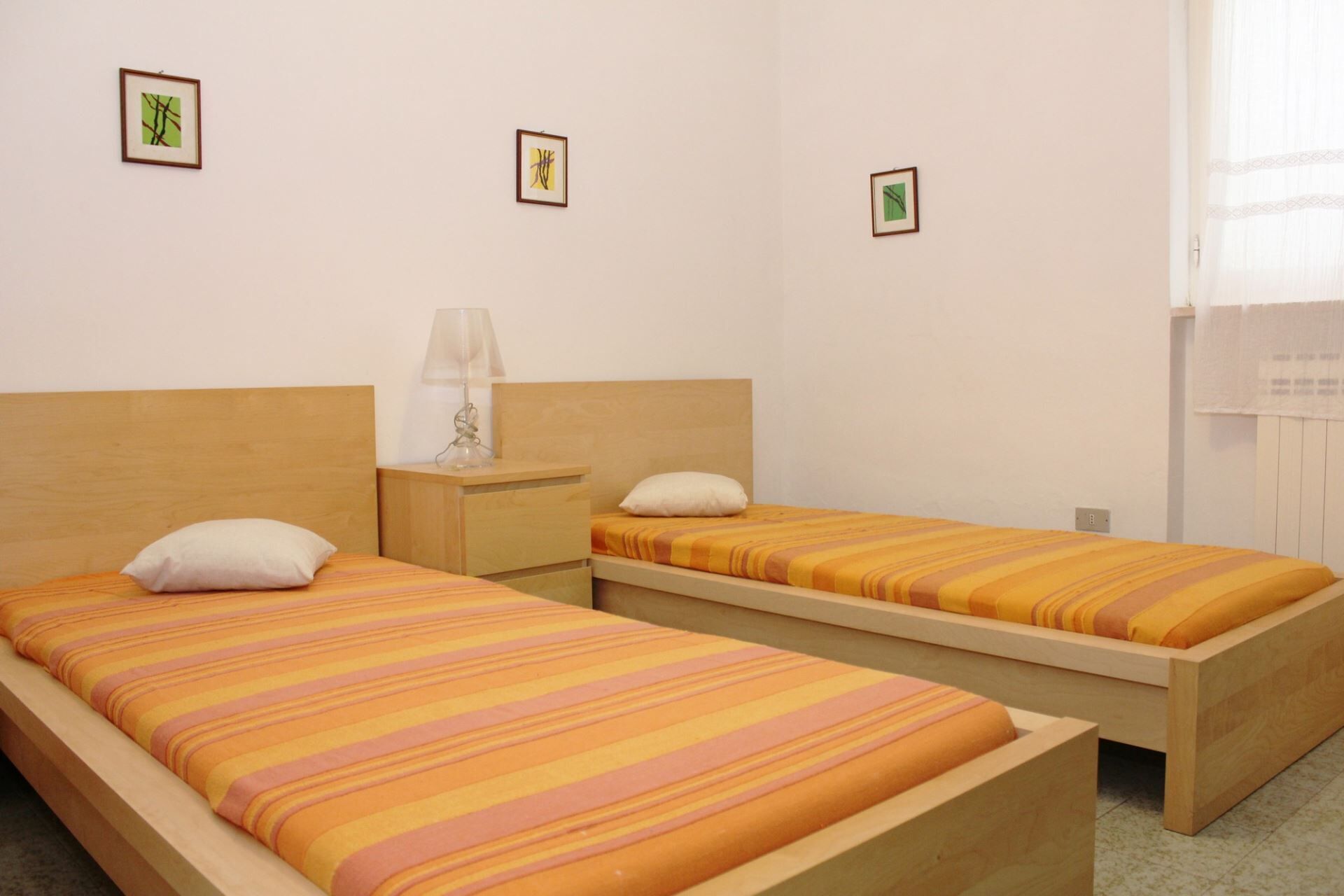 Una habitación con dos camas individuales, una mesita de noche con lámpara y tres cuadros enmarcados en la pared.