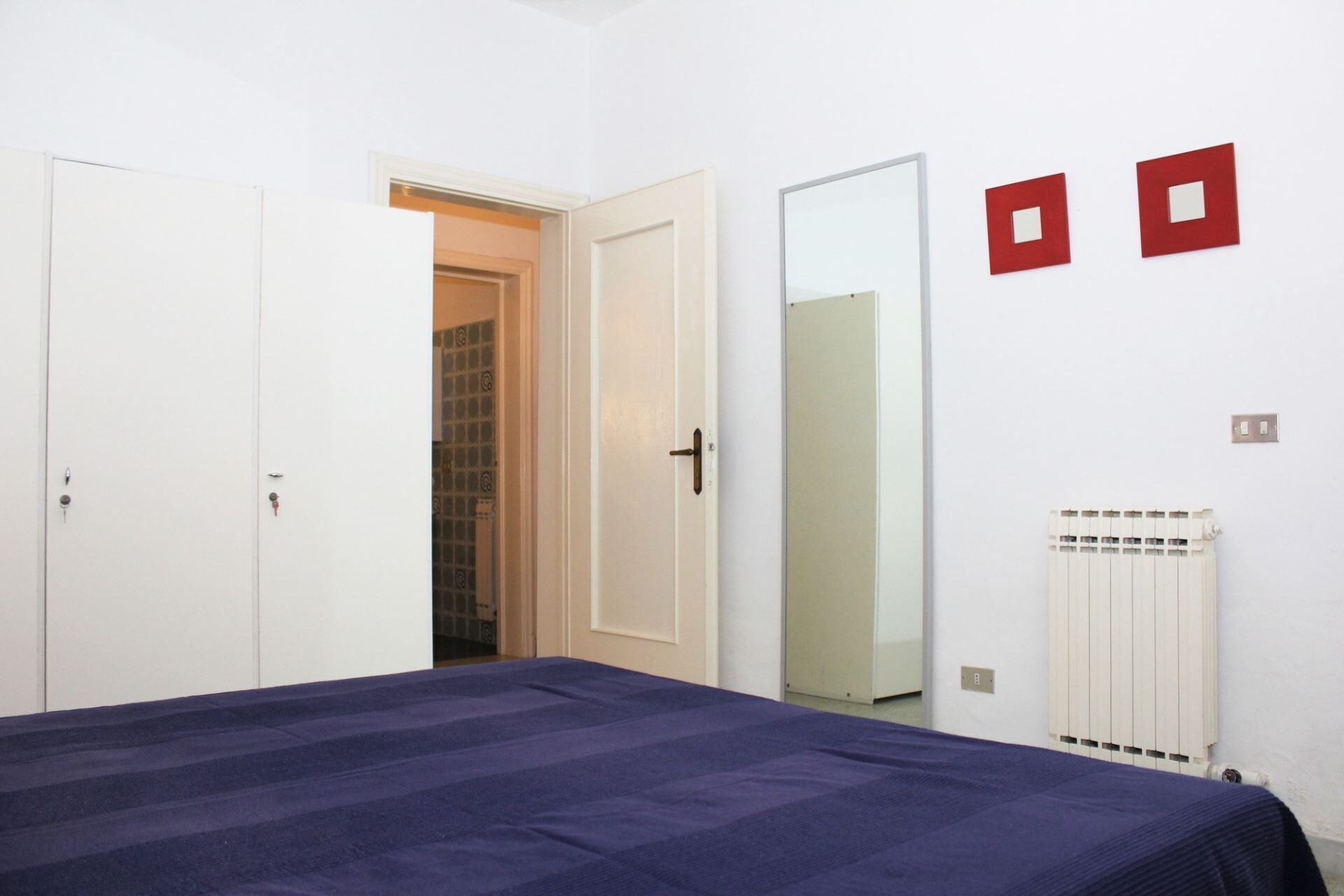 A bedroom with a bed, two doors, a radiator, and a mirror.