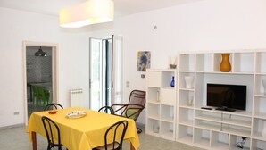A dining area with a yellow table and chairs, a white shelving unit with decorative items, and a television.