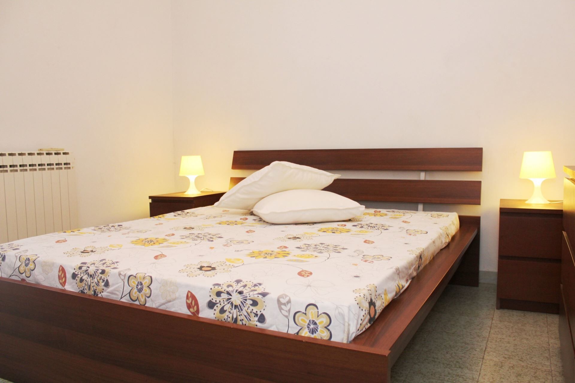 A neatly made bed with a floral bedspread, two bedside lamps, and a wooden headboard.