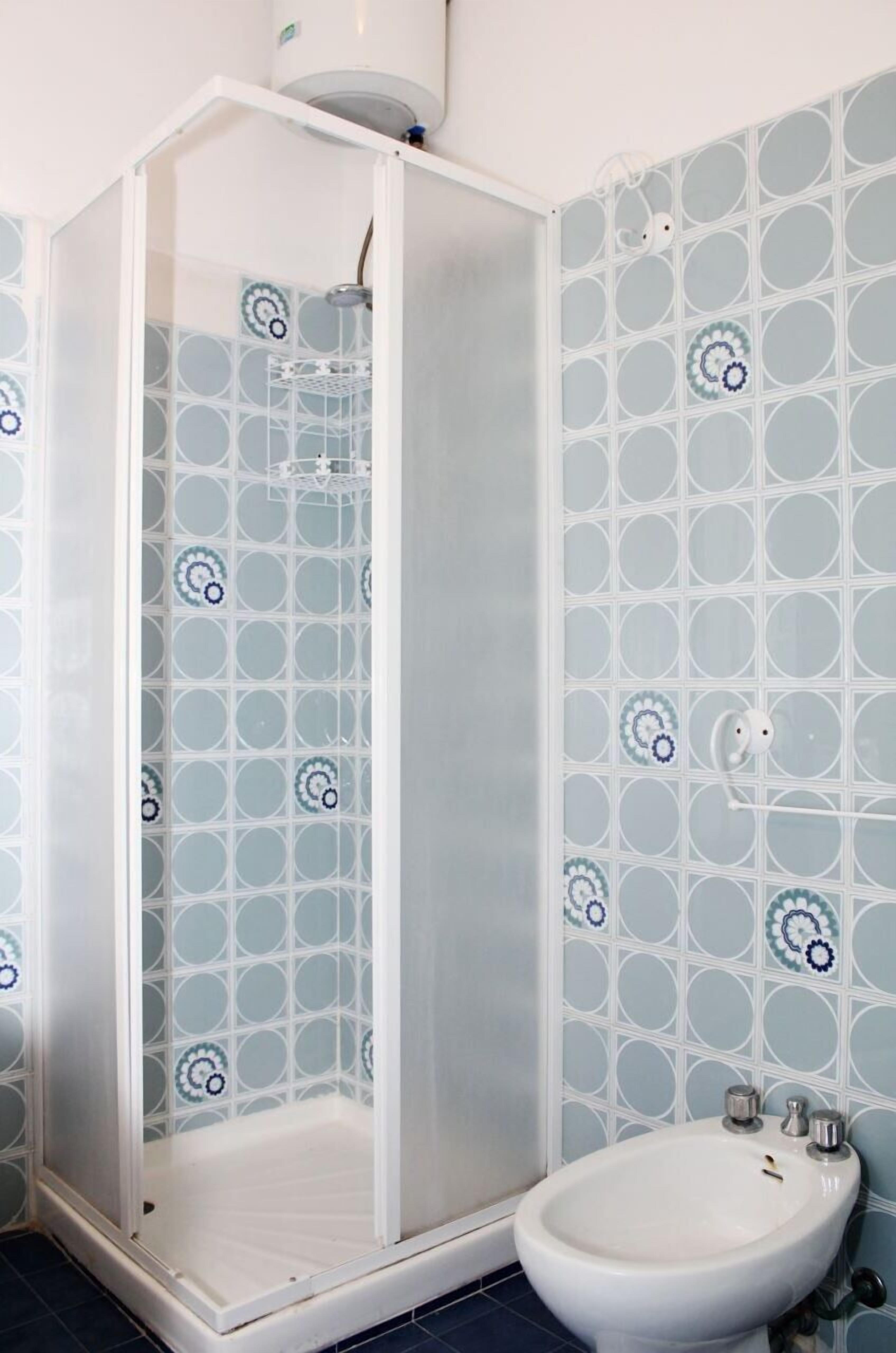 Uma casa de banho com chuveiro em cabine de vidro, pia branca e azulejos estampados nas paredes.