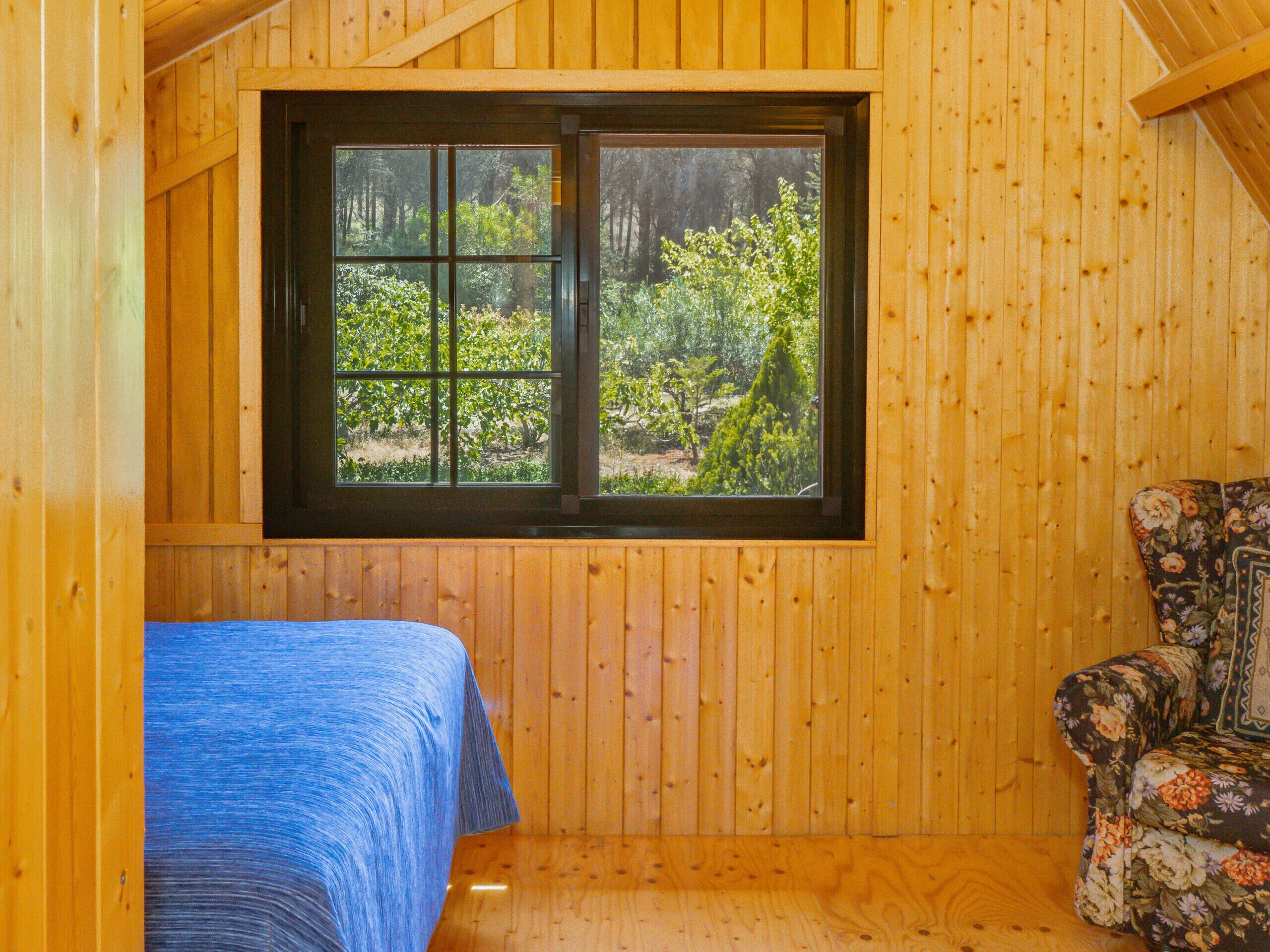 A wooden cabin room with a bed, a window, and a floral-patterned chair.
