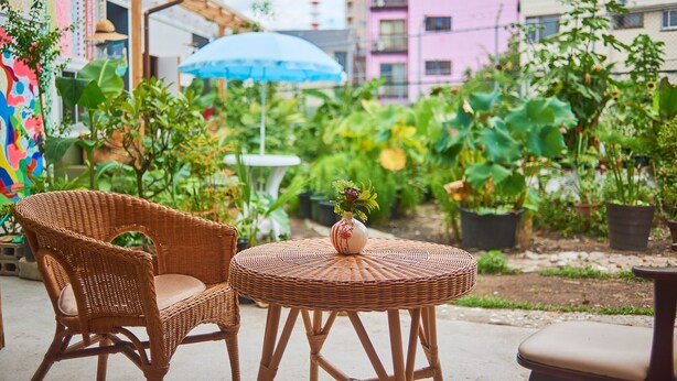 A wicker table and chairs in an outdoor area with potted plants and a colorful mural.
