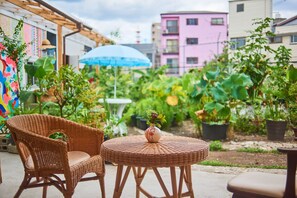A wicker table and chairs in an outdoor area with potted plants and a colorful mural. - Cocoroom Guesthouse Cafe and Garden - Hostel (Osaka)