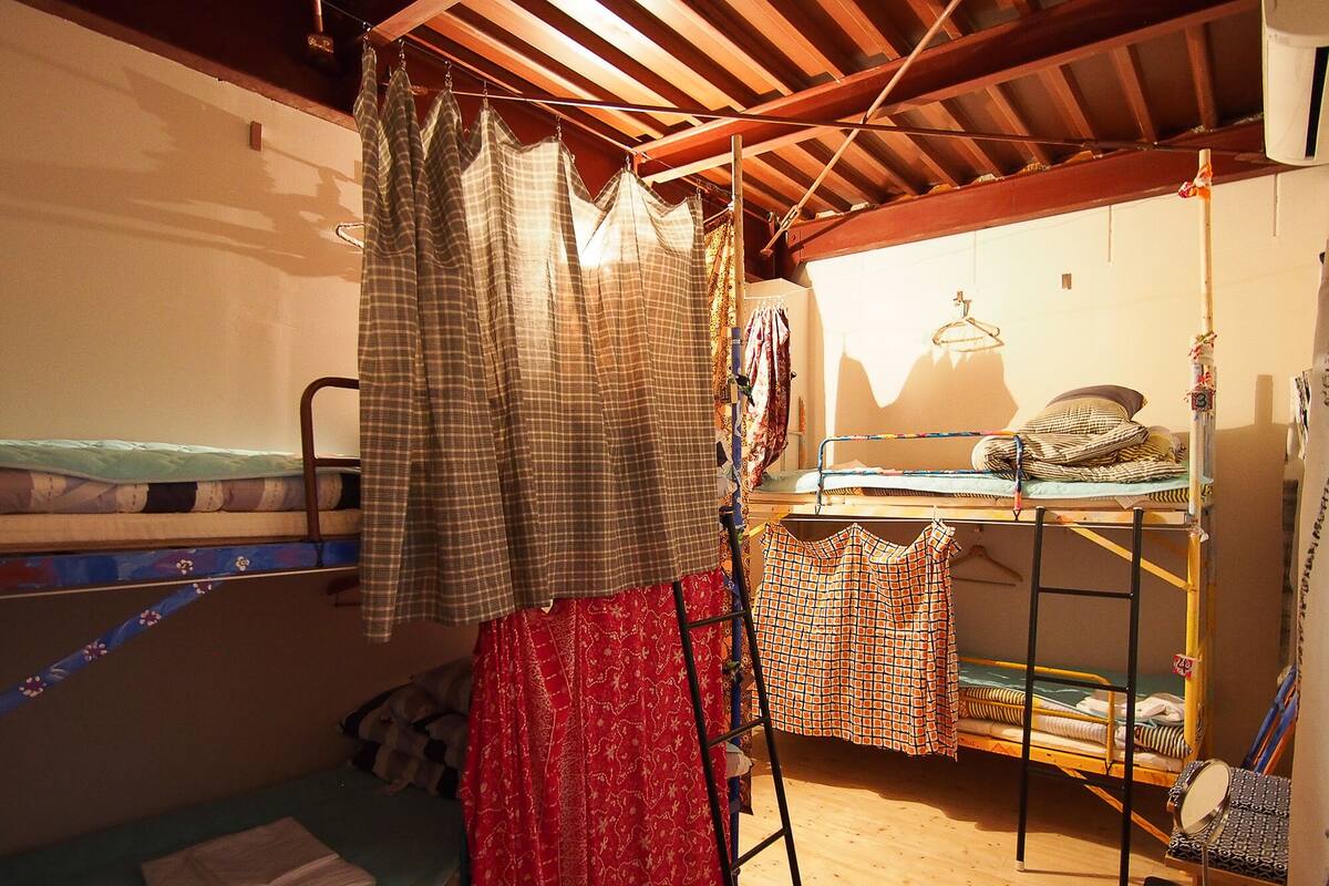 Ein Schlafsaalzimmer mit Etagenbetten, einem kleinen Tisch und einem Kleiderständer mit Kleidung.