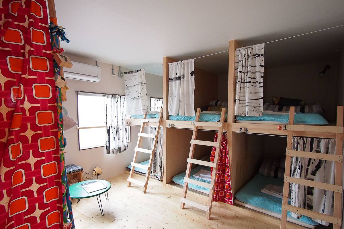 Ein Zimmer mit Etagenbetten, einer Himmelsleiter, einem kleinen Tisch und einem Fenster mit Vorhängen.
