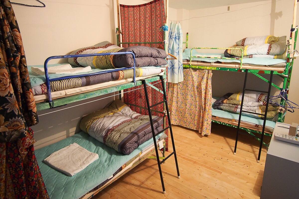 Ein Schlafsaalzimmer mit Etagenbetten, Holzboden und einer Vorhang.