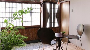 A traditional Japanese room with tatami flooring, a shoji screen, a wooden door, and a small table with chairs.