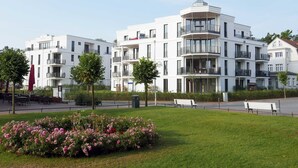 A modern apartment building with multiple balconies and a well-maintained lawn with pink flowers. - Baabe Villen Ensemble FeWo 40 Himmelsnest Ref. 213701 (Baabe)