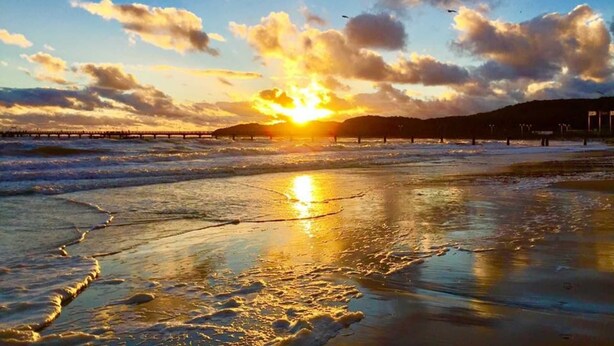 A beach scene with a sunset, waves, and a pier in the background. - Baabe Villen Ensemble FeWo 40 Himmelsnest Ref. 213701 (Baabe)