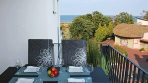 A dining table set with plates, glasses, and a fruit bowl, overlooking a coastal view. - Baabe Villen Ensemble FeWo 40 Himmelsnest Ref. 213701 (Baabe)