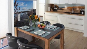 A modern kitchen with white cabinets, a wooden countertop, and a dining area with a table set for two. - Baabe Villen Ensemble FeWo 40 Himmelsnest Ref. 213701 (Baabe)