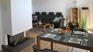 A modern living room with a fireplace, a dining table set for two, and a sofa in the background. - Baabe Villen Ensemble FeWo 40 Himmelsnest Ref. 213701 (Baabe)