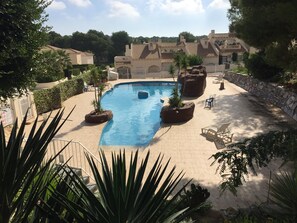 A swimming pool with surrounding lounge chairs and planters, set against a backdrop of buildings and trees. - Superb 3 bedroom apartment in the Golf of Las Ramblas (Orihuela)